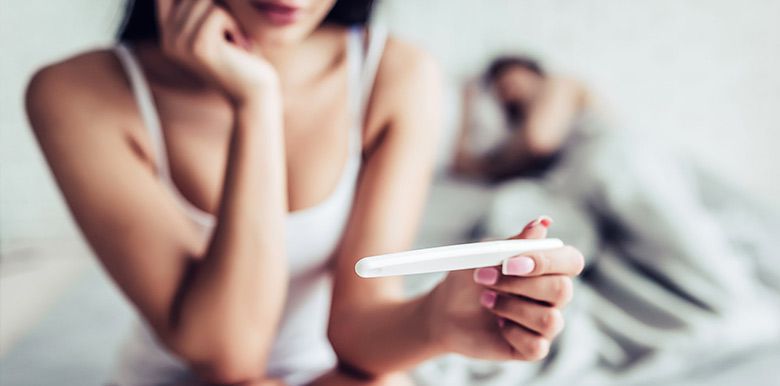 Femme inquiète qui regarde un test de grossesse sur son lit